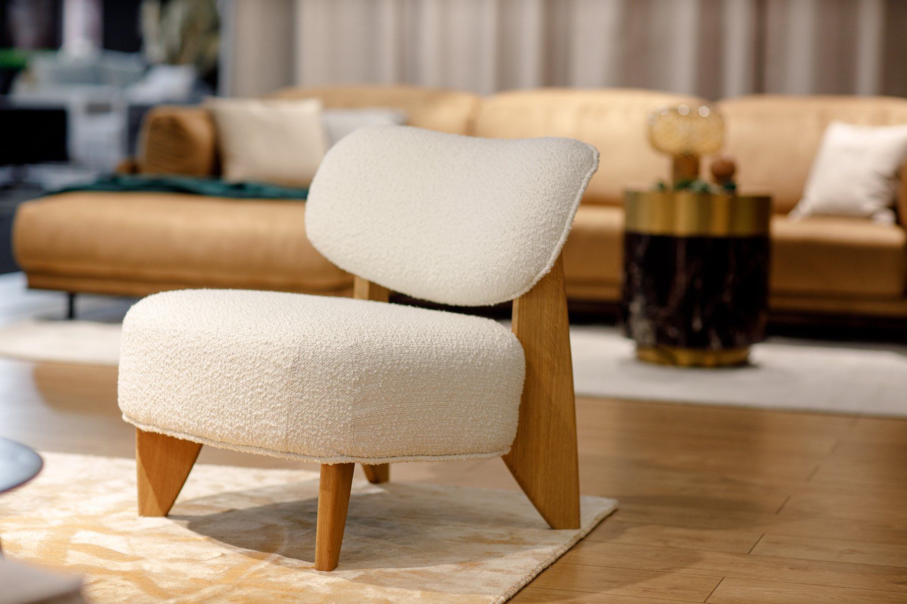 Fotel Juna w kremowej tkaninie bouclé na dębowym stelażu, w tle karmelowa sofa